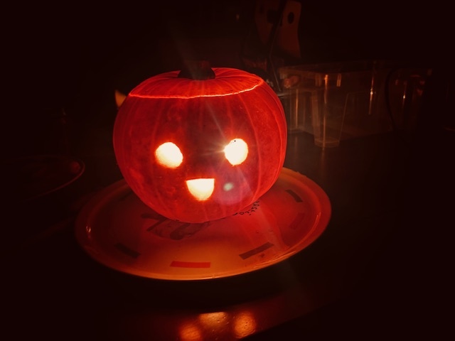 A  candle lit pumpkin with wide open eyes and a happy smiling face in the dark.